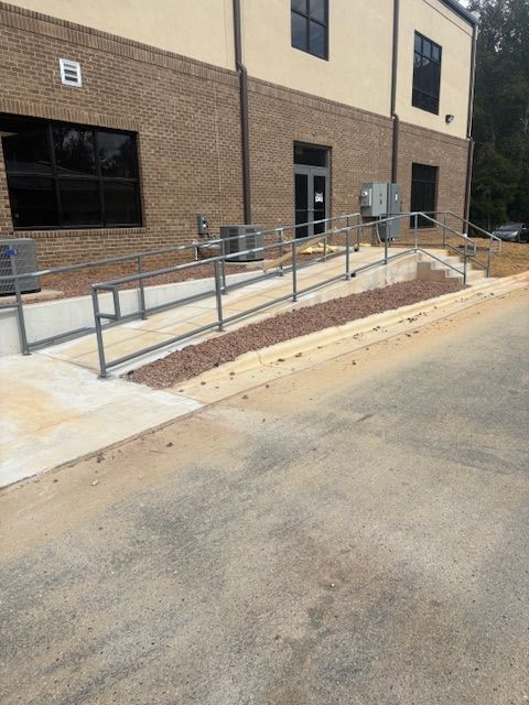 A concrete wheelchair ramp with metal handrails leading to a building entrance with brick and tan exterior walls.