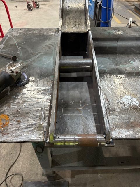 A metal framework assembly rests on a cluttered industrial workshop workbench, featuring welded joints and steel bars.