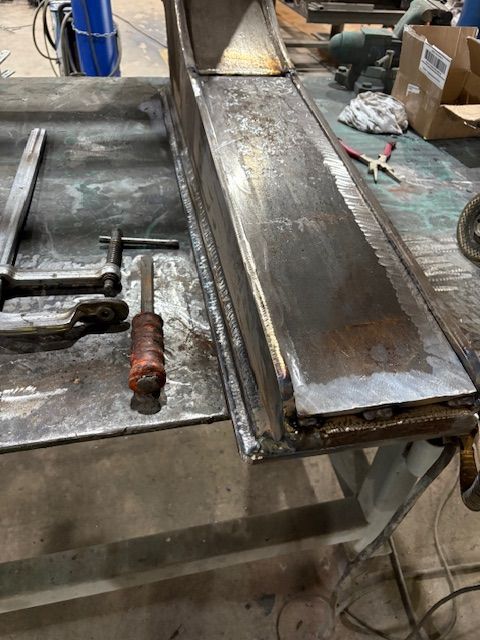 A close-up of a metal welding process, showing sparks and bright light where a rod connects to a dark metal fence frame.