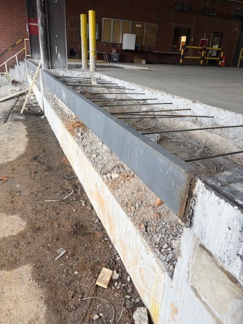 A metal edge guard installed on a concrete loading dock, with exposed steel reinforcement bars extending from the slab.