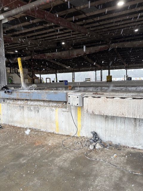 A concrete loading dock with a metal dock plate, yellow safety pillars, and an open, partially covered warehouse interior.