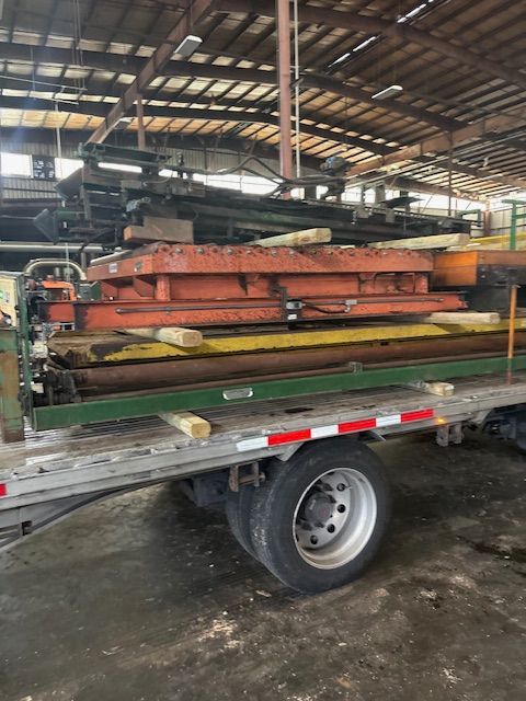 Flatbed trailer loaded with heavy industrial steel machinery, including orange and green beams, in a warehouse setting.