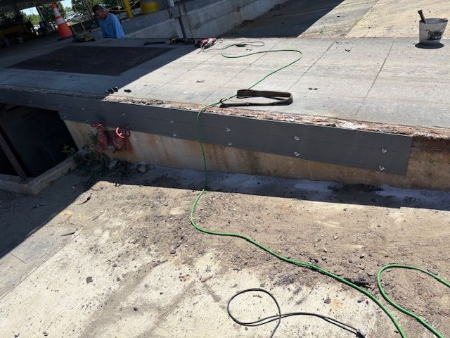 A worker installs a metal edge guard on a concrete loading dock while a power cord lies on the ground nearby.