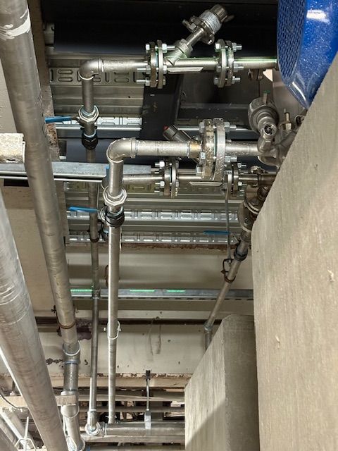 A perspective view of metal pipes and flanged joints mounted to an industrial ceiling.
