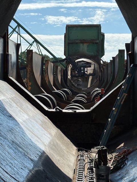 Looking down through a narrow, metal-lined channel toward a circular opening, with an industrial framework visible above.