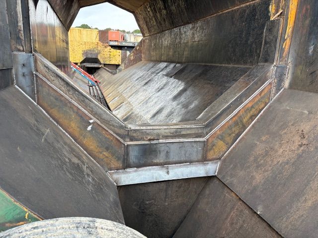A low-angle view inside a large, industrial steel hopper or chute with angled metal panels and welded seams.
