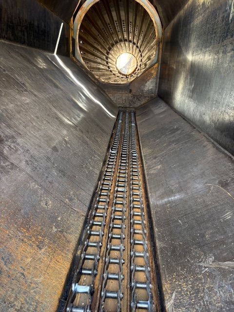 An interior view of a metal chute or industrial hopper, featuring a dual-strand metal chain conveyor along its floor.