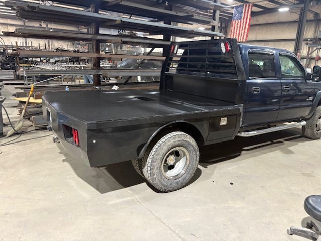 A dark-colored pickup truck with a custom black flatbed utility body parked inside an industrial metal workshop.