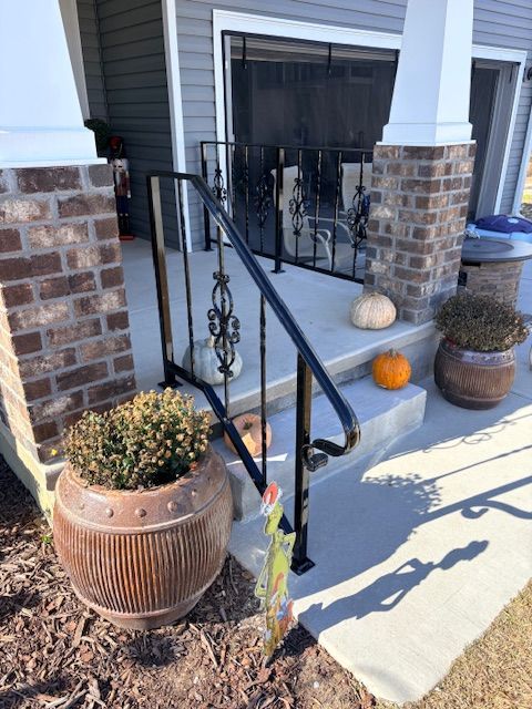 Black metal handrail installed on concrete porch steps, with potted plants and pumpkins nearby.