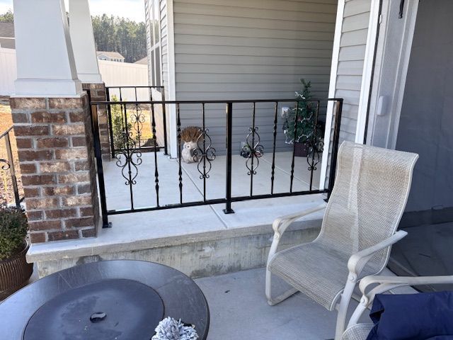 A black wrought iron railing on a concrete porch, featuring decorative scrollwork, with a patio chair in the foreground.