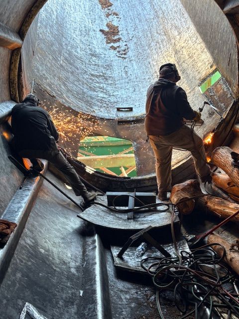 A close-up of a metal welding process, showing sparks and bright light where a rod connects to a dark metal fence frame.