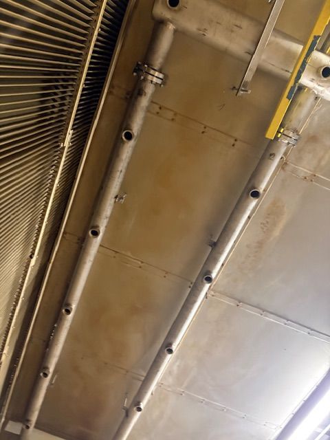 Two parallel metal pipes with regularly spaced circular nozzles mounted on the ceiling of a stainless steel hood.