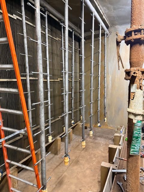 Metal cooling coils or heat exchangers installed in a vertical industrial rack with a water supply pipe in the foreground.