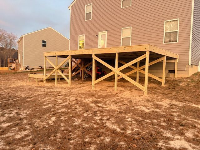 A newly constructed wood deck on the back of a beige two-story house with unfinished ground underneath.