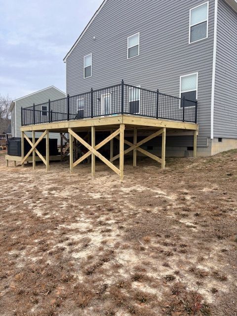 A newly built wooden deck with black metal railings attached to the back of a grey, two-story house.