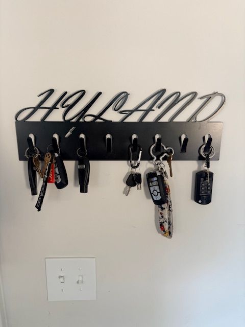 A black metal wall-mounted key rack with the name