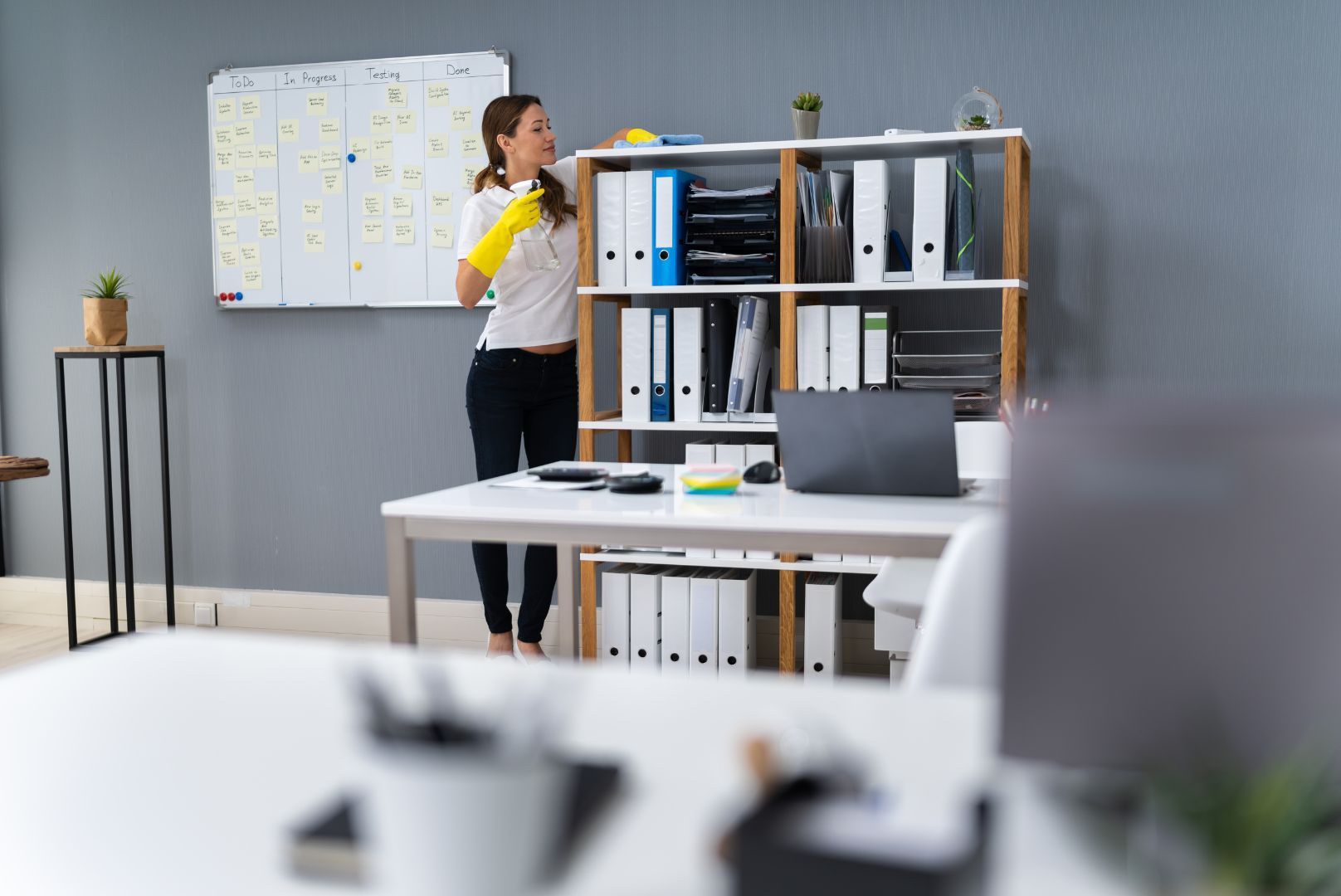 A woman is cleaning an office with a spray bottle.