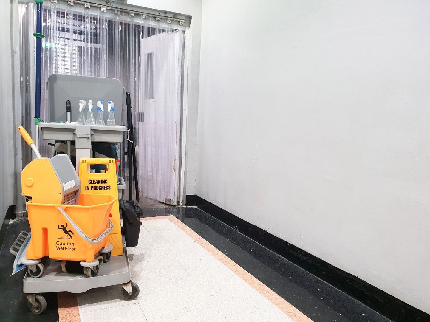 A yellow mop and bucket are sitting on a cart in a hallway.