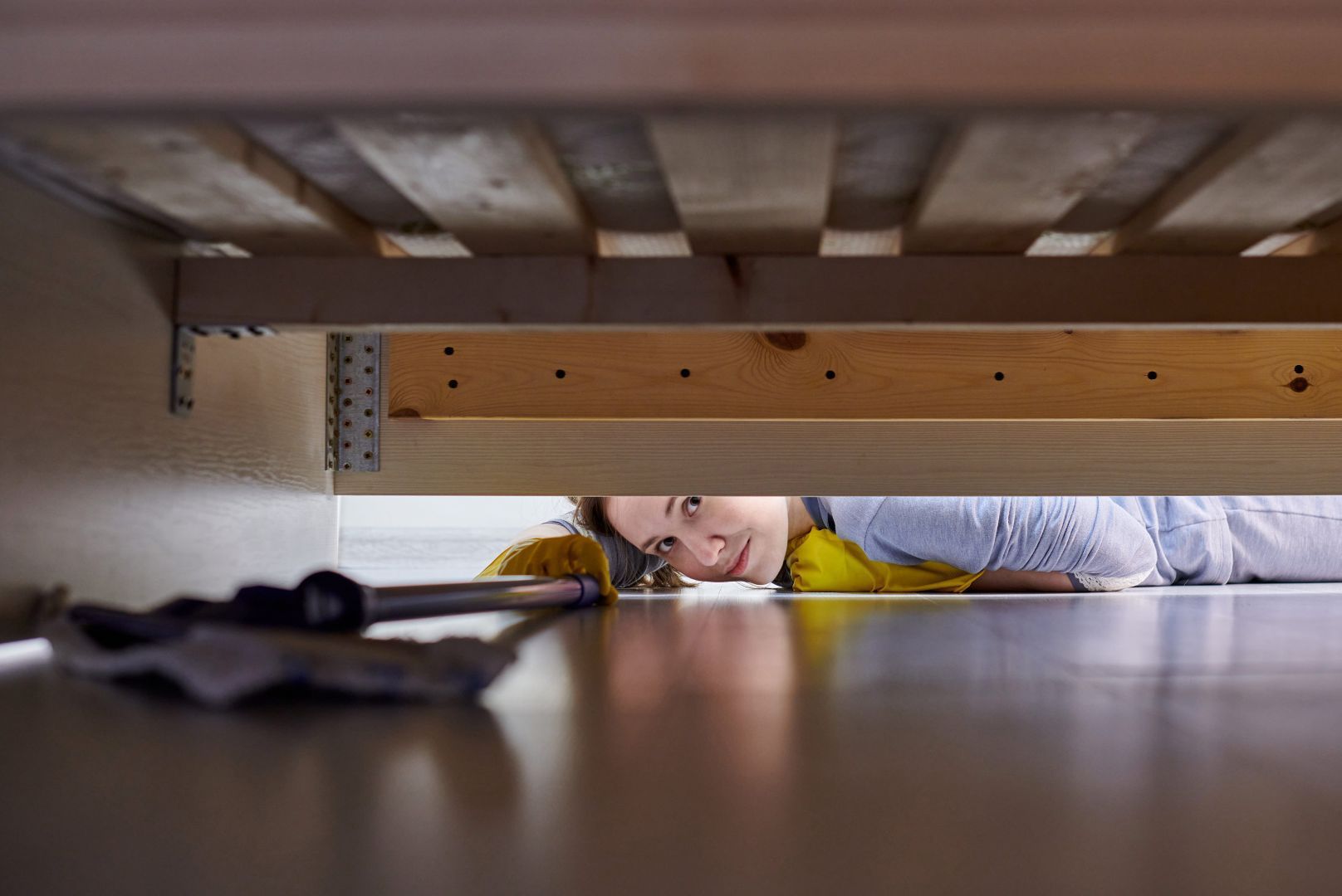 A man is laying under a bed with a screwdriver.