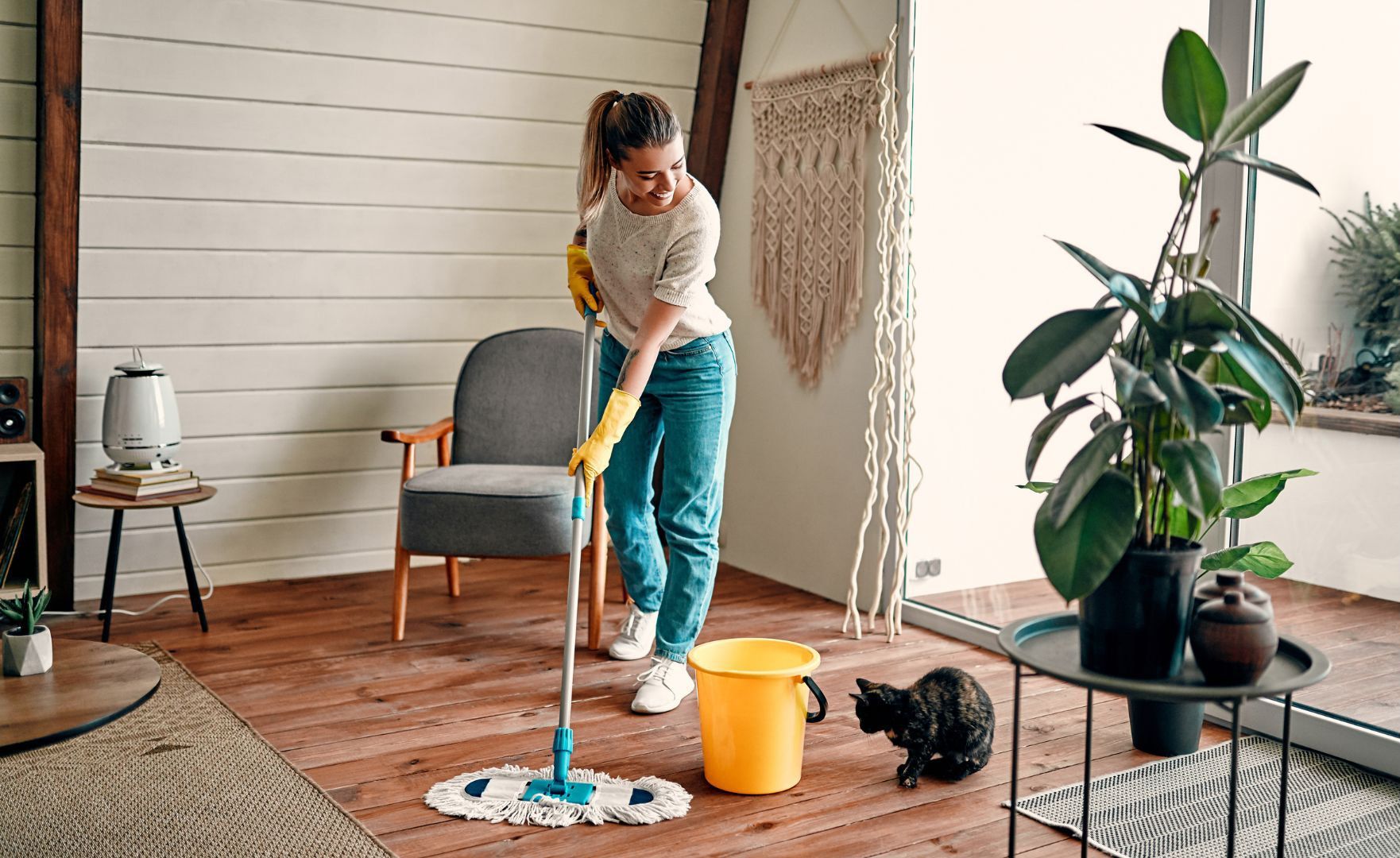 A woman is cleaning the floor in a living room with a mop and bucket.