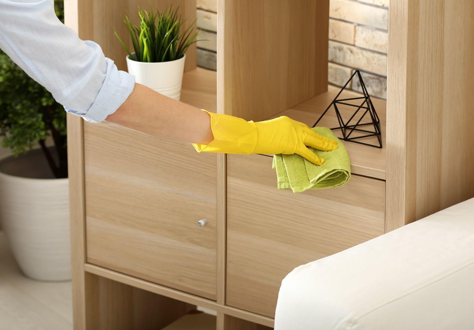 A person wearing yellow gloves is cleaning a wooden shelf with a cloth.