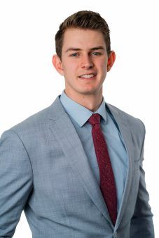 Young man in a light blue suit and burgundy tie smiling at the camera.