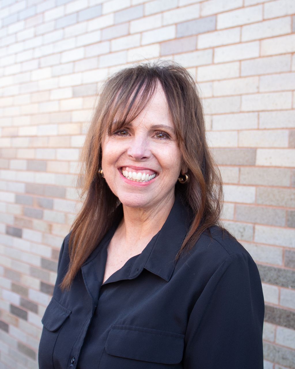 Woman smiles at the camera in front of a brick wall, wearing a black shirt.
