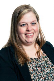 Woman with blonde hair smiles, wearing a black blazer over a patterned top.