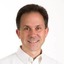Man in white shirt smiling at the camera against a white backdrop.
