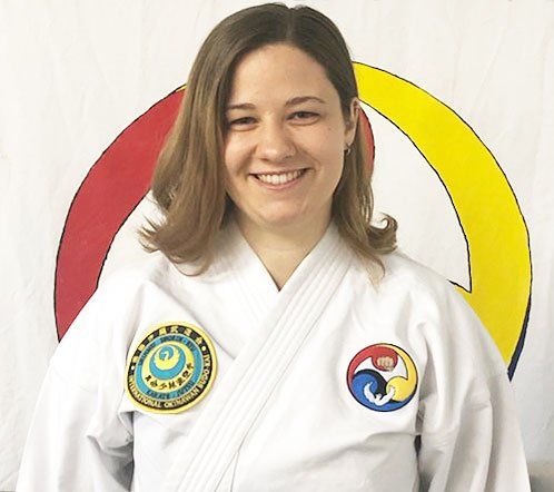 A woman is wearing a white karate uniform and smiling