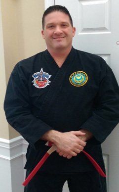 A man in a black karate uniform is holding a red belt