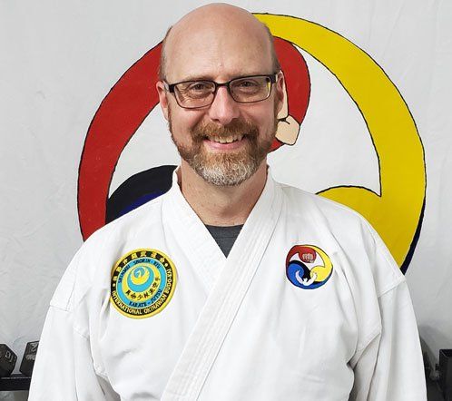 A man wearing a white karate uniform and glasses is smiling for the camera.