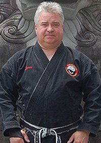 A man in a black karate uniform is standing in front of a statue.