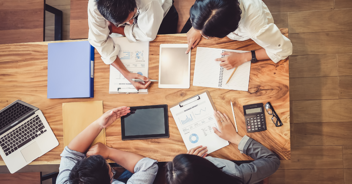 4 people sitting at a desk with papers and tablets