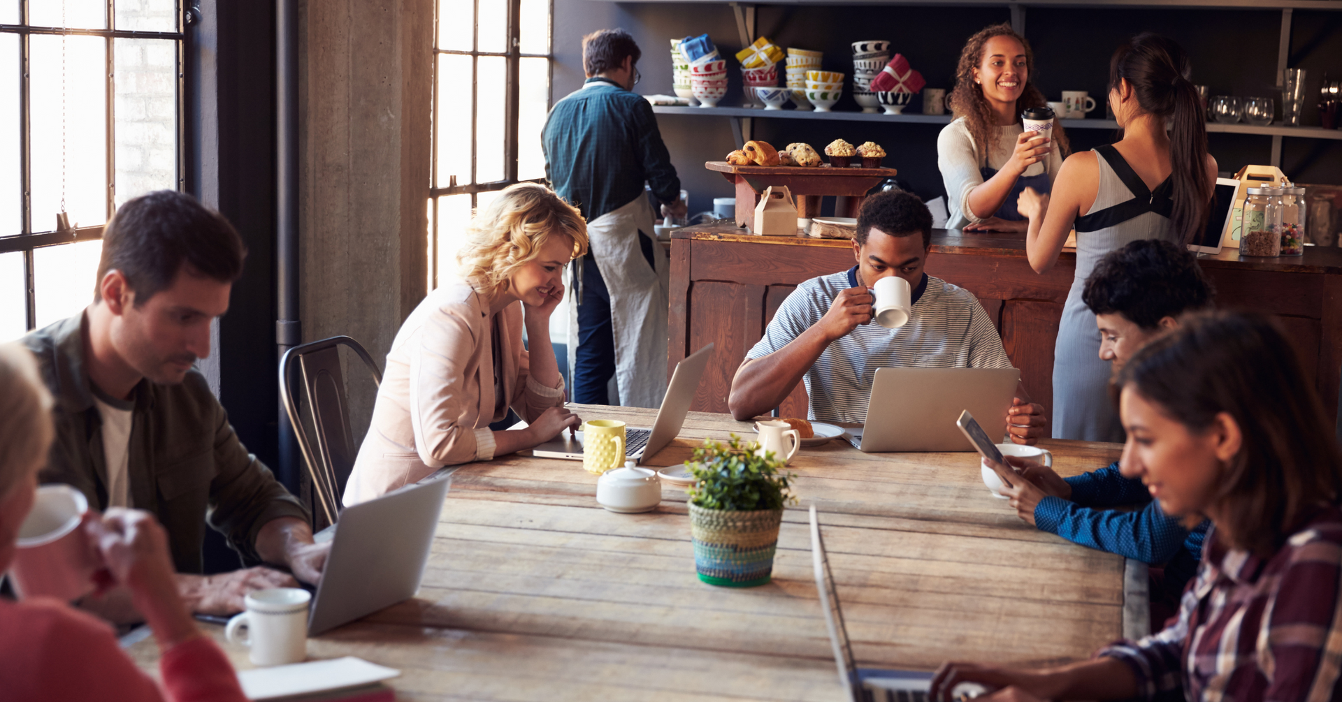 people working on laptops and drinking coffee out of mugs at a coffee shop