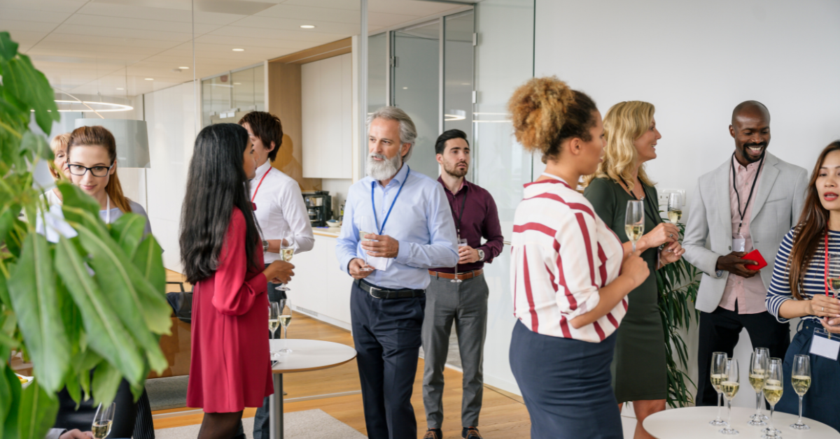  A diverse group of professionals casually networking in a modern coworking office, holding drinks and chatting during a social or business event.