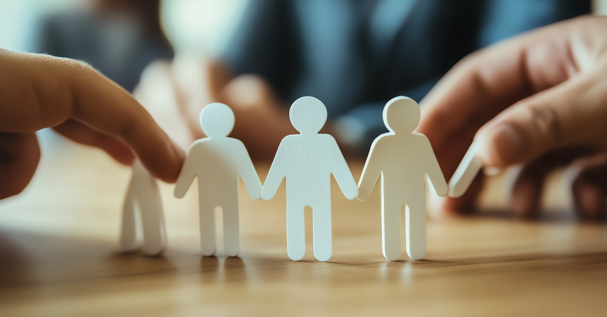 Hands arranging paper people figures to represent teamwork, collaboration, and employee connection during business planning