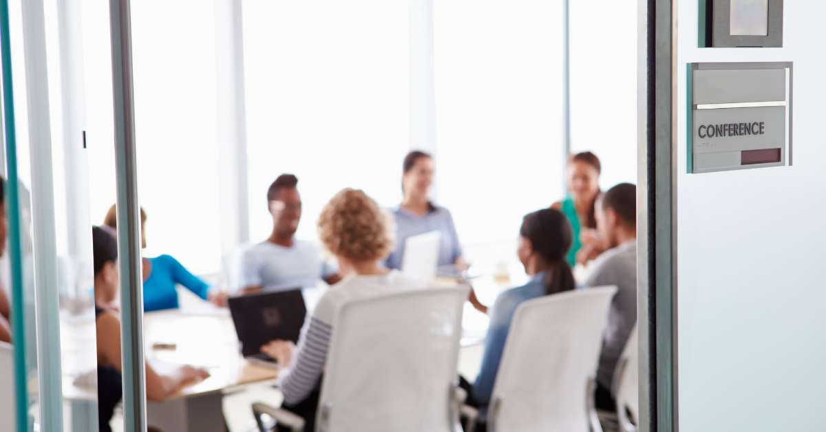 Diverse team of professionals in a glass-walled conference room engaged in discussion around a table