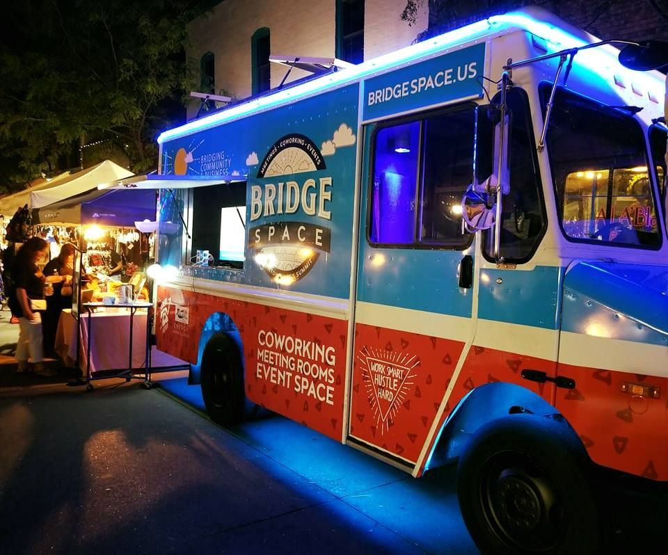A bridge space food truck is parked on the street at night