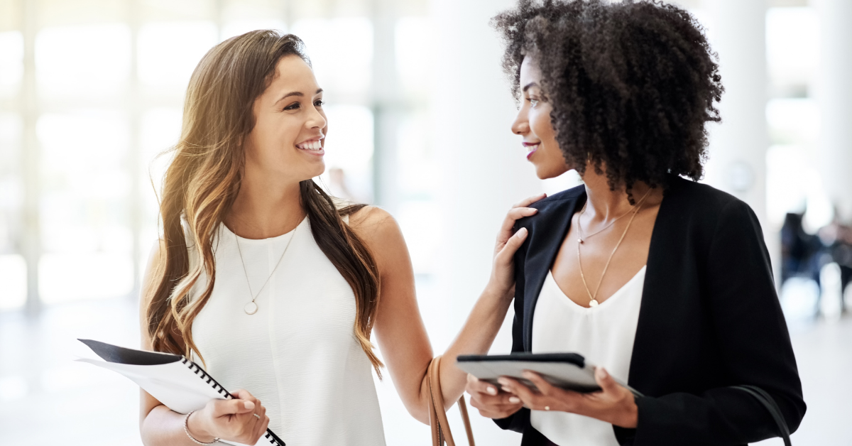 Two professional women having a business discussion in a bright modern coworking space, smiling