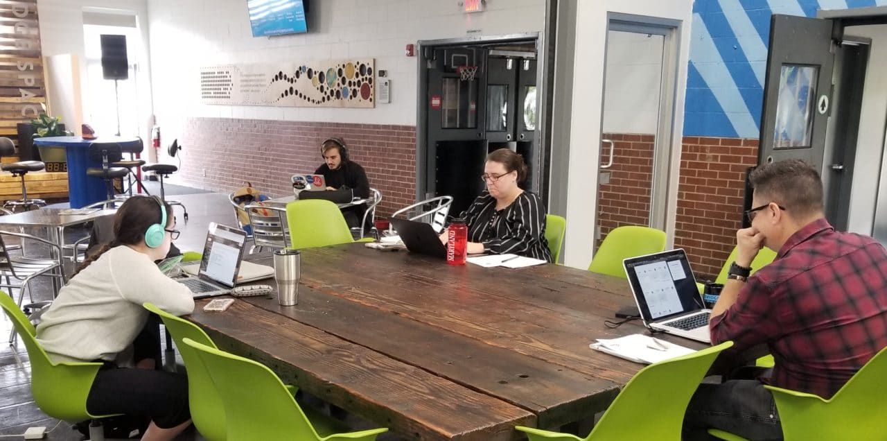 A group of people are sitting around a table with laptops.