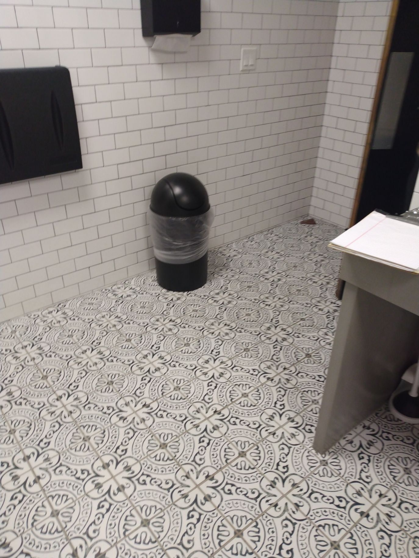 a black trash can sits on a tiled floor in a bathroom