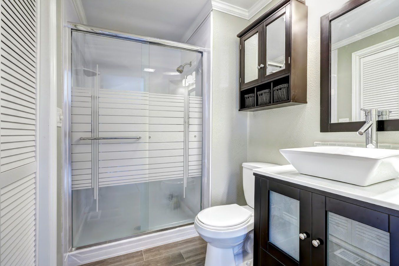 A bathroom with a toilet , sink , mirror and shower stall.