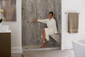 A woman is sitting on a bench in a shower in a bathroom.