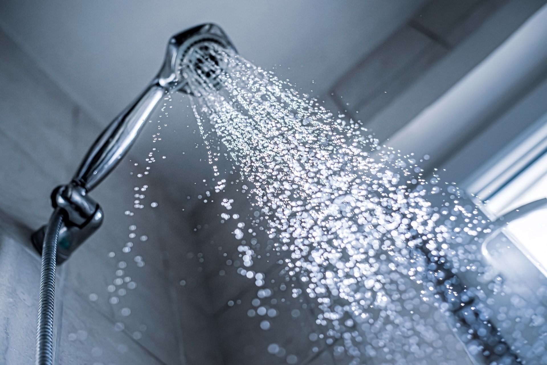 A shower head, inside a bathroom, as it expels water.