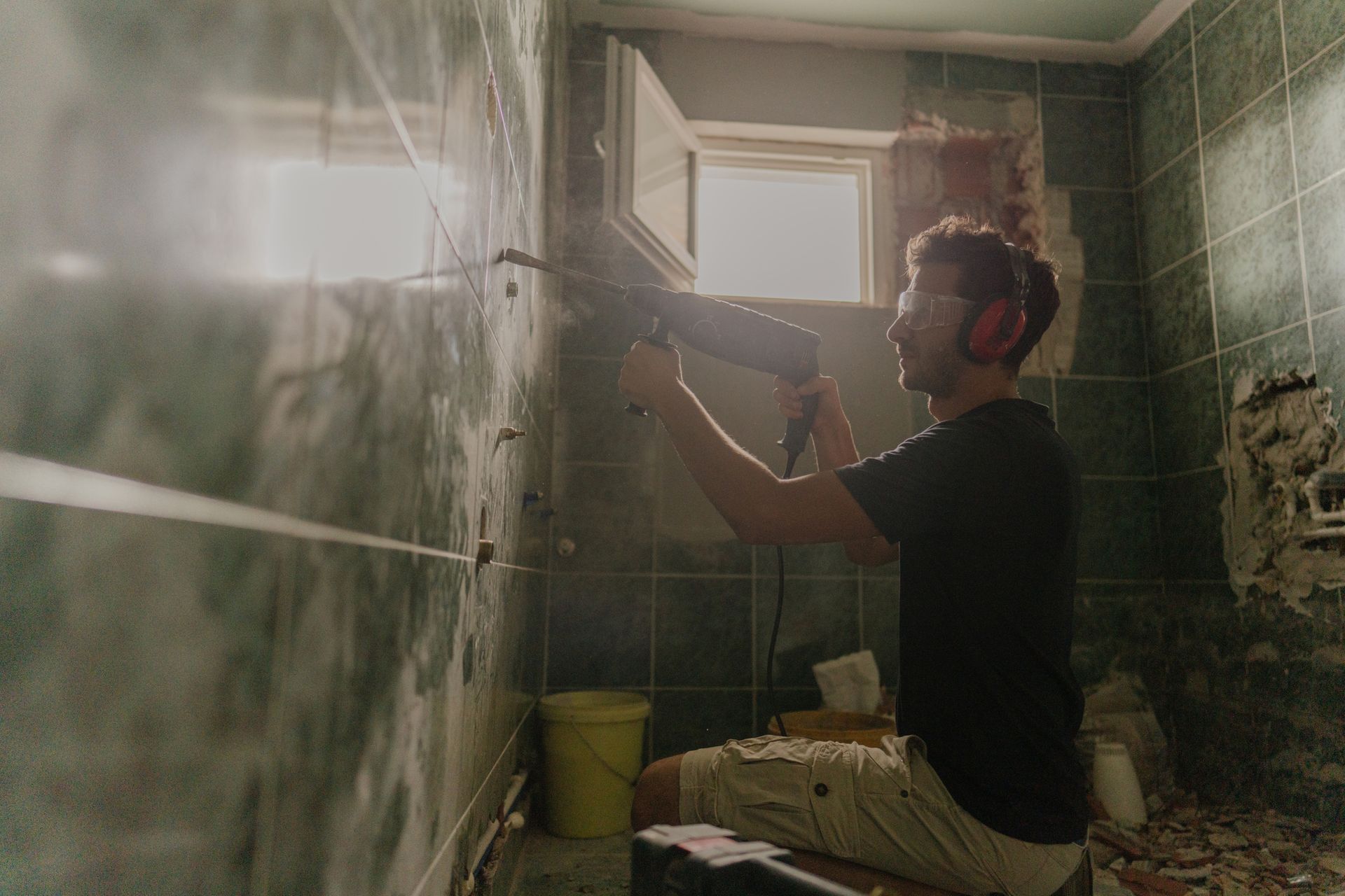 A worker wearing glasses uses a power drill while working on a bathroom remodeling project.