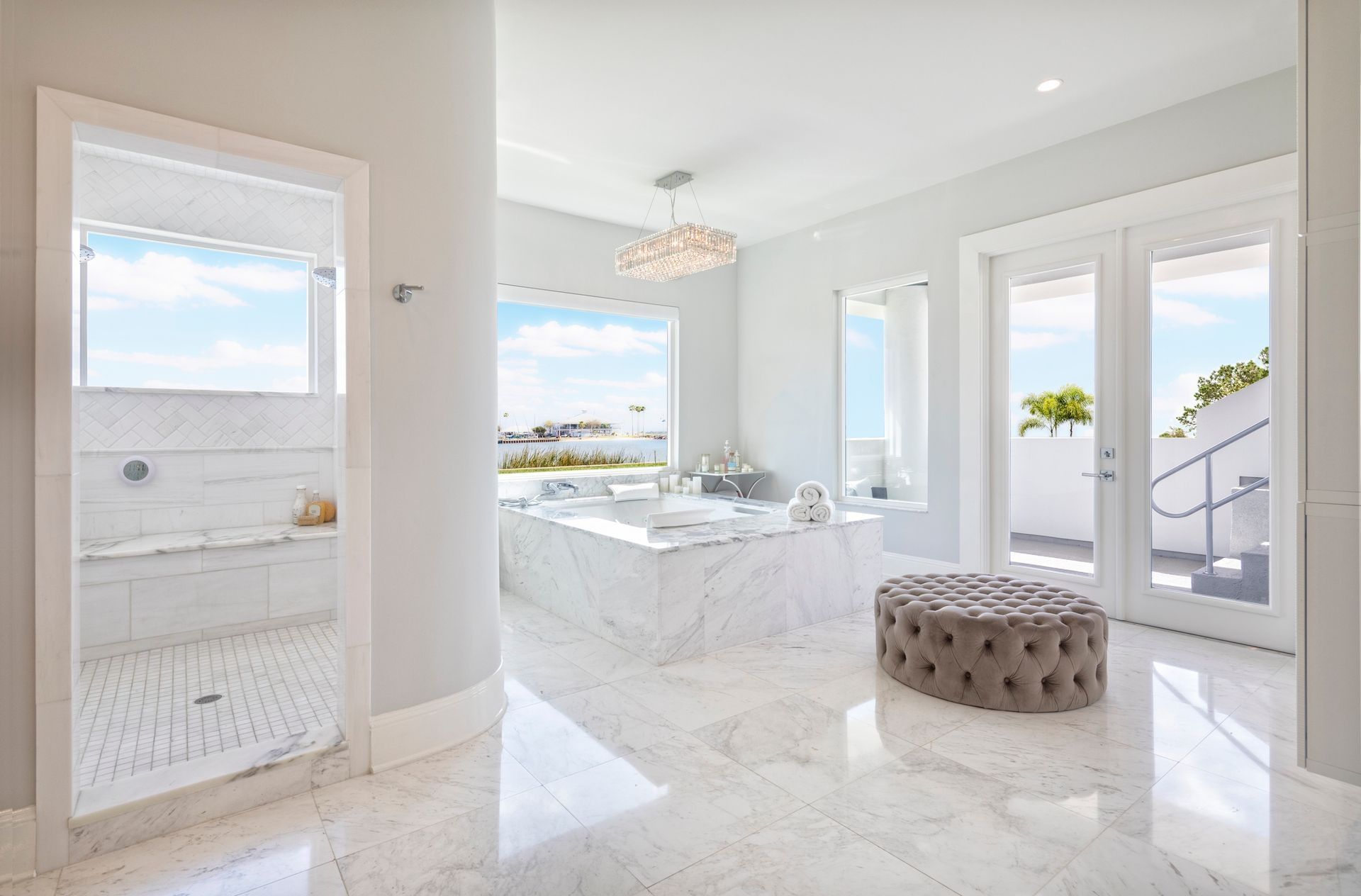 A bathroom with two sinks , two mirrors and a walk in shower. A bathroom with a large tub and a ottoman in it.