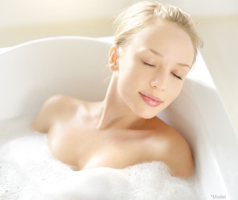 Woman relaxing in a bubble bath, eyes closed, smiling, in a white bathtub.