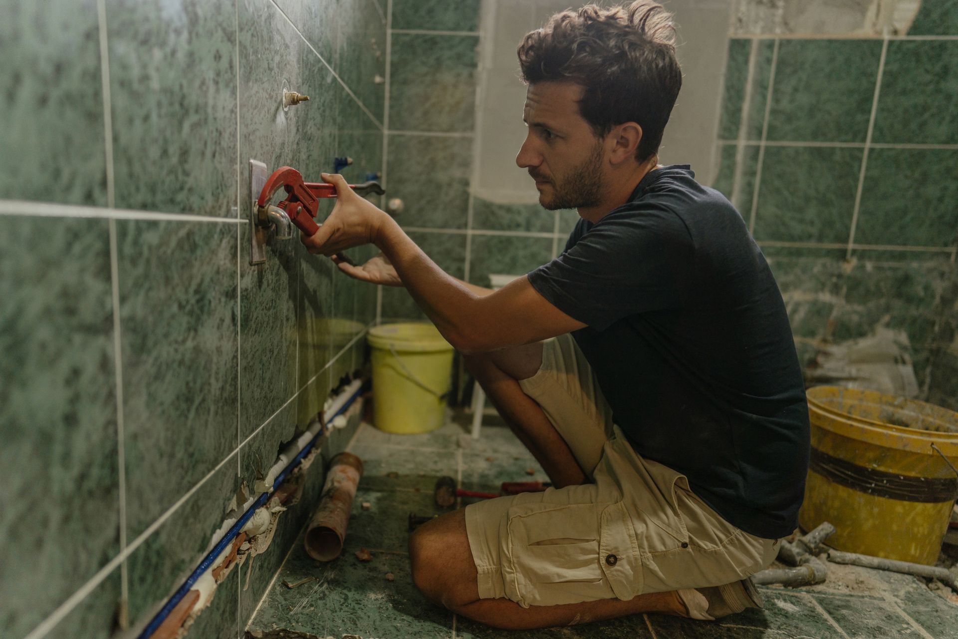 A worker uses a wrench while working on the plumbing during a bathroom remodeling project.