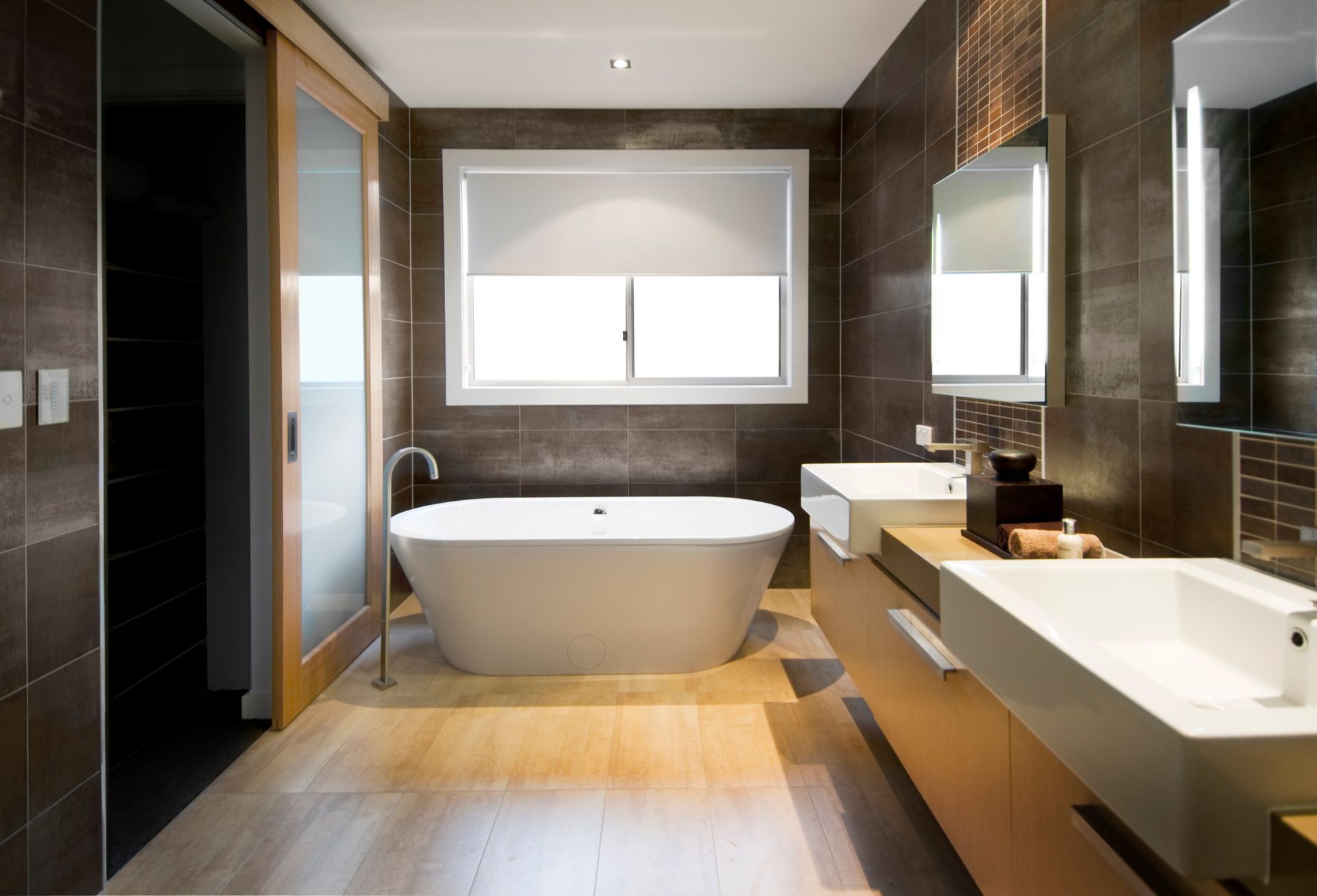 A bath with freestanding tub, brown tiles, and hardwood floors highlighting bathroom remodeling.